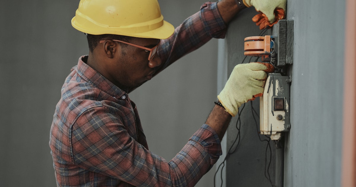 HVAC technician in hard hat and safety gear installing equipment on a residential unit