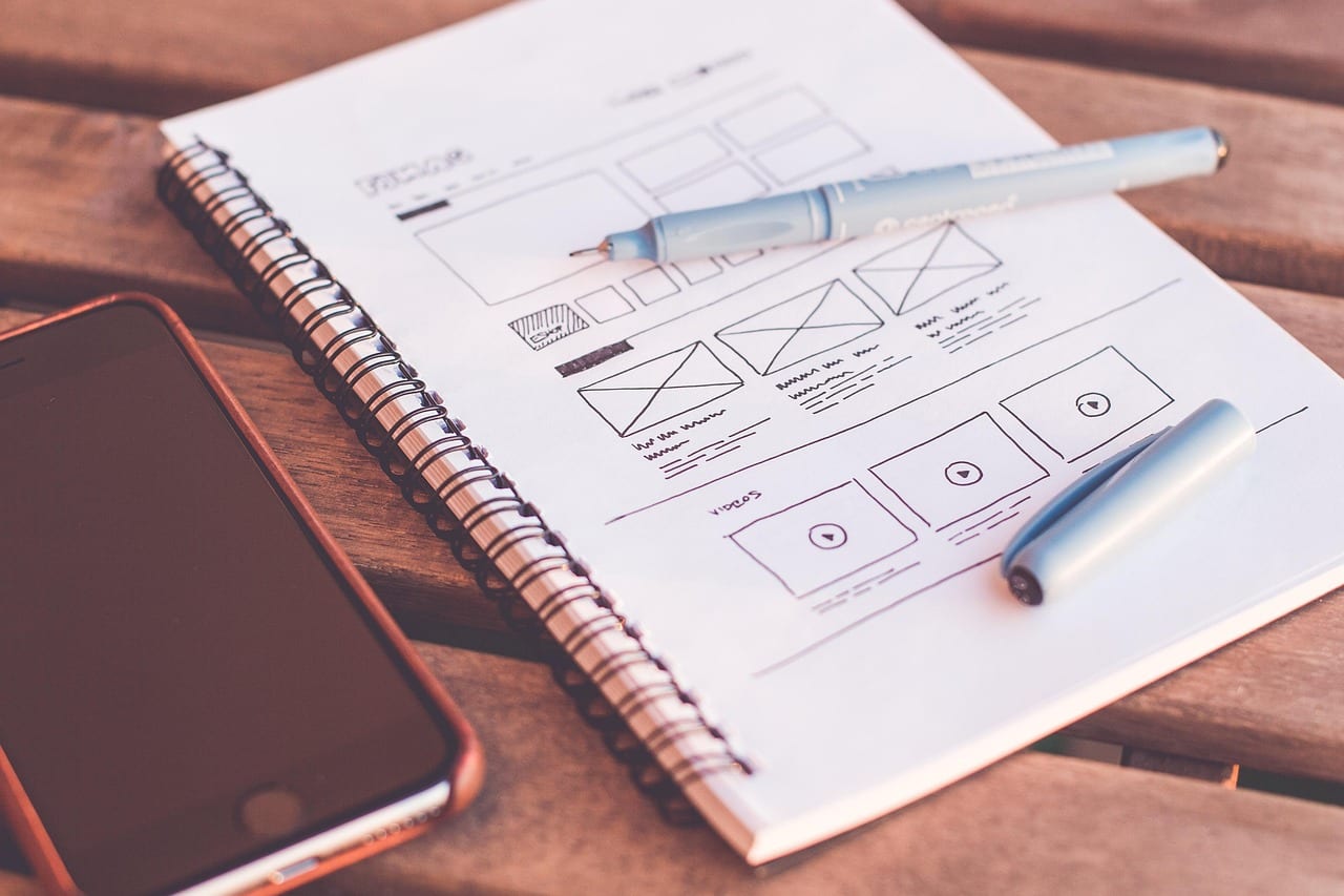 UX designer sketching mobile wireframes at a desk surrounded by layout prototypes